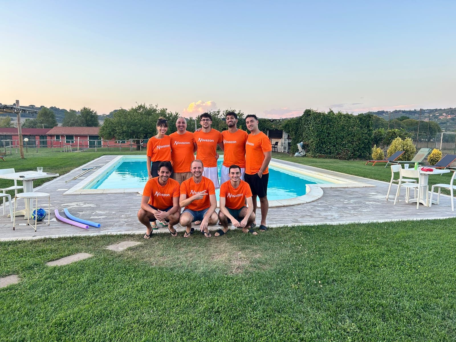 The whole Novazon team by the pool at sunset, in orange team t-shirts